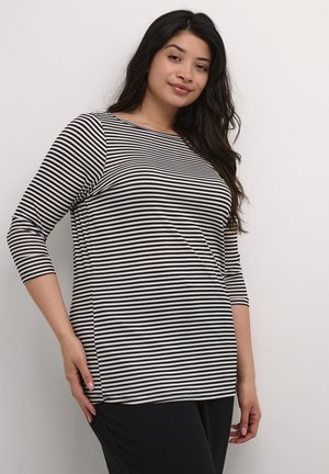 Black and white striped long-sleeve top with a rounded neckline and side slits, worn with black pants. Smooth fabric, relaxed fit.