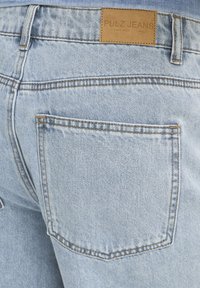 Hellblaue Jeans aus Denim mit einer Gesäßtasche und einem braunen Lederetikett mit der Aufschrift "PULZ JEANS" am Bund.