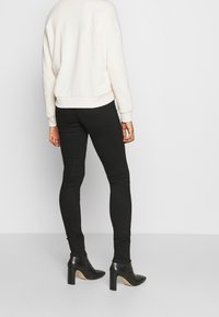 Sudadera de crema con un corte relajado, combinada con jeans negros ajustados y botines de tacón alto negros, fotografiada desde atrás.