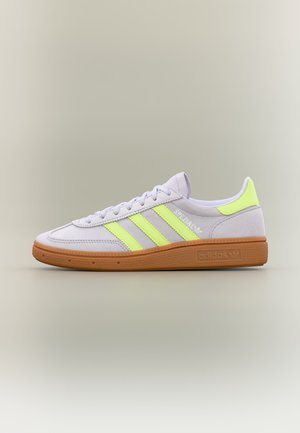 Baskets blanches Adidas avec bandes jaunes néon et détail au talon, semelle en caoutchouc marron, coupe basse et marquage "Spezial" sur le côté.