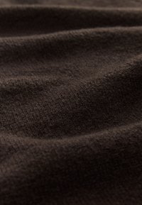 Ruskea teksturoidun kankaan pinta on pehmeä ja uritettu, jossa näkyy hienovaraisia ryppyjä ja vaihtelevia tummanruskean sävyjä ympäriinsä.