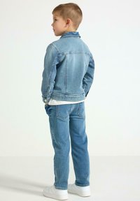 Jeansjacke in Hellblau, mit klassischem Schnitt, Knopfakzenten und sichtbaren Nähten; kombiniert mit passenden hellblauen Jeans und weißen Sneakern.