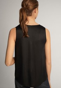 Haut noir sans manches avec une texture lisse et mate, et un ourlet arrière arrondi. Design simple, sans motifs visibles ni détails métalliques.