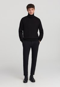 Czarny sweter z golfem w zestawieniu z czarnymi, dopasowanymi spodniami i czarnymi sznurowanymi butami. Prostym, teksturowany wzór dzianiny z ściągaczami przy mankietach.