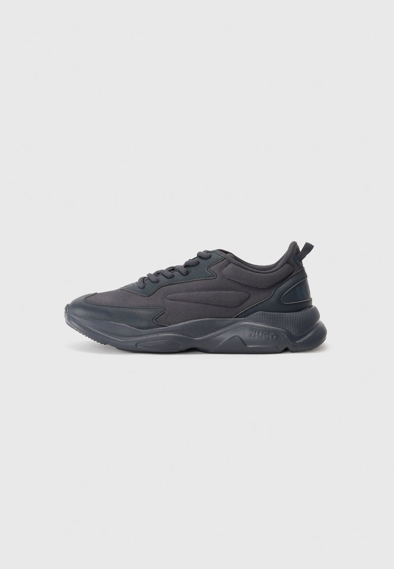 Black athletic shoes with a mesh and synthetic upper, featuring a rounded toe, textured sole, and prominent brand logo on the heel.