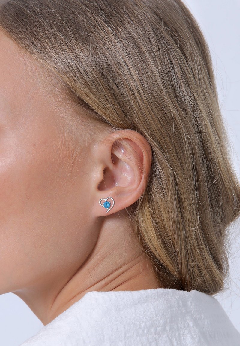 Silberne herzförmige Ohrringe mit einem blauen Edelsteindetail. Glatte Oberfläche, kleine Größe, geeignet für legere oder formelle Anlässe.