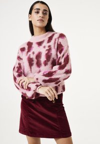 Fluffy roze trui met onregelmatige bordeauxrode vlekken, ronde halslijn en lange mouwen, gecombineerd met een bordeauxrode ribfluwelen rok met knopen aan de voorkant.