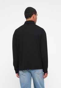 Polo a maniche lunghe nera con una morbida consistenza e vestibilità comoda. Presenta un colletto piegato ed è abbinata a jeans in denim azzurro chiaro.