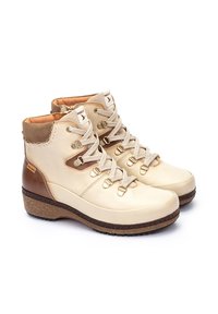 Bottines en cuir beige avec un accent en daim marron, bout rond, matériel doré et semelle texturée. Affiche un design à lacets et un col rembourré.