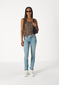 Leopard print tank top, light blue skinny jeans, white sneakers, and a black handbag. Model has long braids and sunglasses.