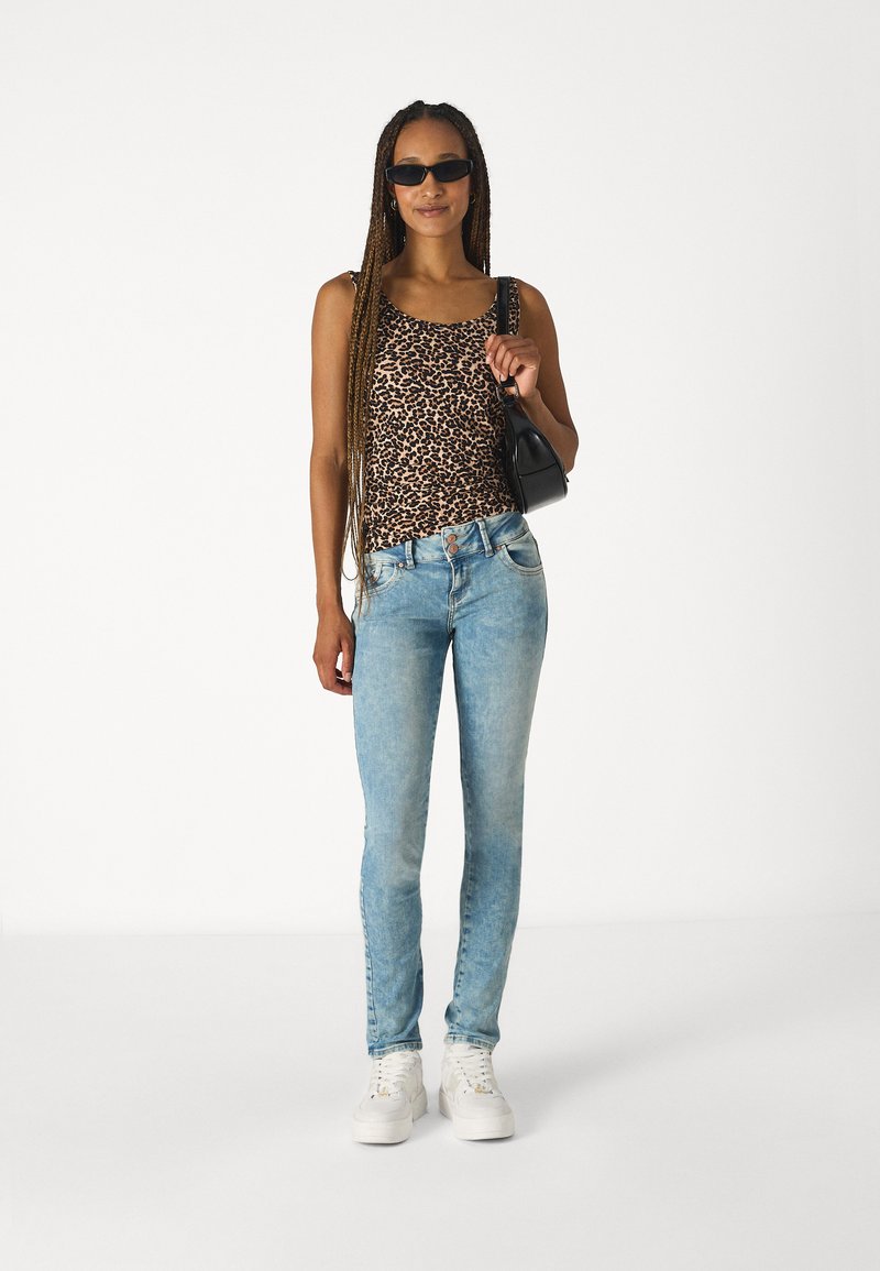 Leopard print tank top, light blue skinny jeans, white sneakers, and a black handbag. Model has long braids and sunglasses.