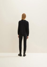 Maglietta nera a maniche lunghe con colletto arricciato, abbinata a pantaloni scuri aderenti e stivaletti neri. Design minimal con una silhouette pulita.
