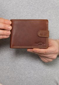 Hnědá kožená peněženka se šitými okraji a západkovým uzávěrem. Na přední straně má debossované logo a hladký povrch.