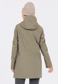 Olijfgroene waterdichte jas met een capuchon, lange mouwen en een rechte snit. Geribbelde beige gebreide muts op het hoofd.