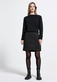 Mustaa neulepaitaa ja tummanharmaata hametta on yhdistetty mustiin nilkkasaappaisiin. Tekstuurit näyttävät pehmeiltä, sopivaltuista muotoilusta ja minimalistisesta tyylistä.