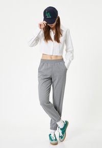 Pantalones de chándal grises con puños elásticos, una camisa corta blanca con botones, y una gorra azul marino con el texto "Los Ángeles". Unos sneakers verdes y blancos completan el atuendo.