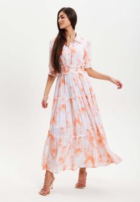 Long, button-up dress in white with orange tie-dye patterns. Features short, puffed sleeves and tiered ruffles at the hem. Lightweight fabric.
