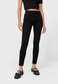 Zwarte denim skinny jeans met een hoge taille, met vijf zakken en een subtiele textuur, gecombineerd met zwarte loafers met zilveren accenten.