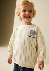 Světlé béžové mikina s modrými pruhy, zdobená plyšovou aplikací slona a textem "AHOJ KAMARÁDE". Žebrované manžety a lem.