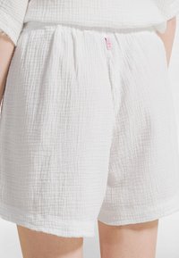 Zbliżenie osoby noszącej białe teksturowane bawełniane szorty z elastyczną talią i małą różową metką z tyłu.