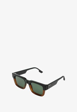 Lunettes de soleil carrées avec montures en plastique noires et brunes, verres teintés en vert et branches angulaires. Présente des accents métalliques.