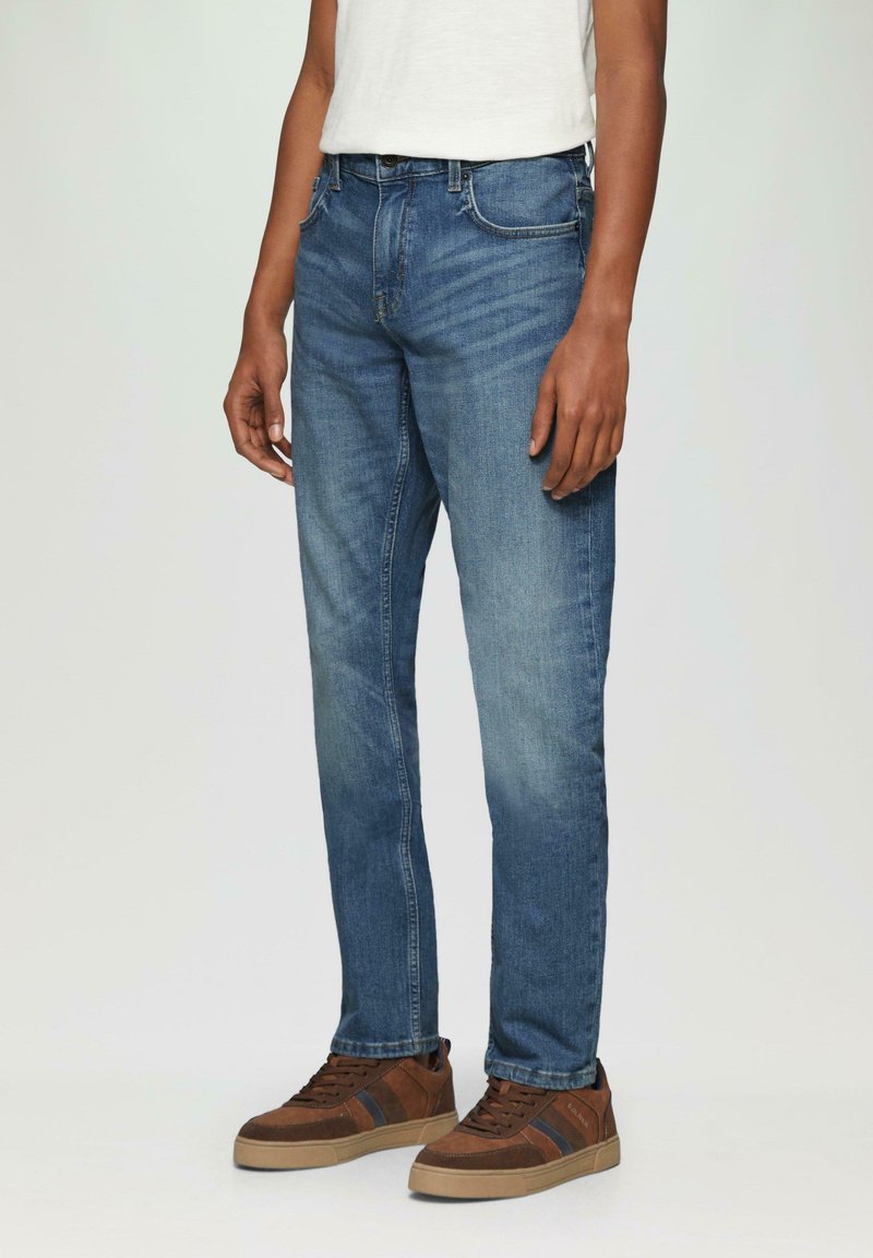 Donkerblauwe denim jeans met een rechte snit, vervaagde secties, vijf zakken en een knoopsluiting, gedragen met bruine en beige sneakers.