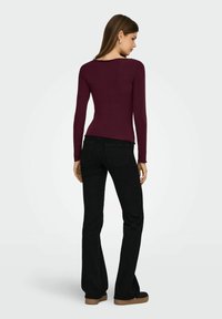 Burgundy lange mouwen top met een ronde hals, gecombineerd met zwarte flared jeans en zwarte plateau schoenen. Zachte textuur, aansluitend design.