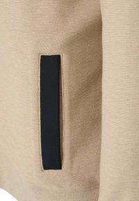 Beige sweatshirtstof met een gestructureerd oppervlak, voorzien van een donkerblauwe opgestikte zak aan de linkerkant.