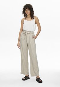 Pantalons larges en lin léger beige avec une taille à nouer et des poches latérales, associés à un débardeur blanc et des sandales noires.