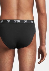 Slip in cotone nero con una larga vita elastica che presenta il logo "CR7" in bianco. Texture liscia, design aderente e stile minimalista.
