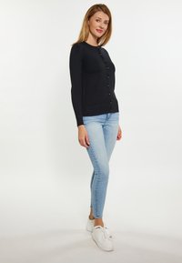 Mustat pitkähihaiset neuletakki, jossa on pyöreä kaula-aukko, etupuolella napitus, ribbireunus. Takki on yhdistetty vaaleansinisiin slim fit -farkkuihin ja valkoisiin lenkkareihin.