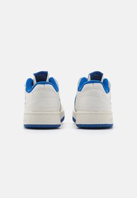 White sneakers with blue accents, leather upper, padded collar, textured sole, and logo detail on the heel. Suitable for casual wear.