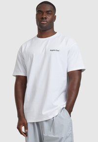 Valge lühikeste varrukatega t-särk ümmarguse kaelusega, mille vasakus rinnaosas on musta tikandiga kiri "unustatud näod".