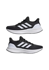 Paire de chaussures de course Adidas noires et blanches avec trois bandes et semelles blanches épaisses vues de côté sur fond blanc.