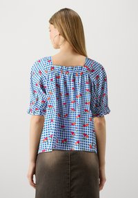 Blusa in gingham azzurro con stampa floreale rossa; maniche corte a palloncino, scollatura quadrata e dettaglio arricciato sul retro; tessuto di cotone leggero.