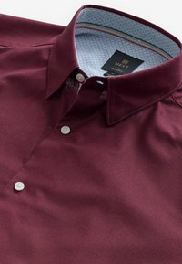 Cămașă burgundy cu guler tip button-down, având un căptușel interior cu model albastru. Textură netedă, cu nasturi albi și detalii de cusătură subtile.