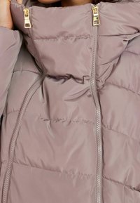 Close-up of mauve puffer jacket featuring two vertical gold zippers and quilted stitching.