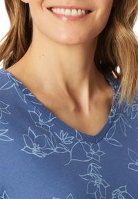 Blauser mit V-Ausschnitt in Hellblau mit floralem Muster, glatter Textur und lockerer Passform, die den Ausschnitt und die Schulterpartie betont.