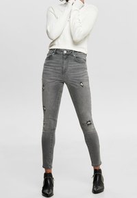 Jeans grises de tiro alto con detalles desgastados, con forma ajustada y una textura suave de denim. Combinados con botines negros.