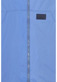 Jachetă de culoare albastru deschis, cu un fermoar frontal și un suport texturat, un mic patch negru pe piept și material neted cu un finisaj mat.