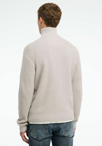 Gai krēmkrāsa, ribota augsta kakla džemperis ar garām piedurknēm un pieguļošu apakšmalu. Teksturēta dzijas dizains papildina brīvo siluetu.