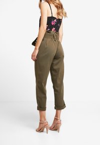 Olivgröna byxor med avslappnad passform, med uppvikta fållar och hög midja. Kombineras med nude-färgade klackar och en blommig topp.