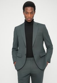 Γκρι σακάκι με δύο κουμπιά και πέτο με εγκοπή, σε συνδυασμό με μαύρο ζιβάγκο. Λείο ύφασμα με εφαρμοστή γραμμή.