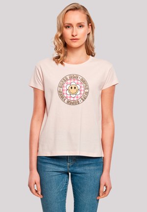 Light pink cotton t-shirt with short sleeves, featuring a graphic design of a smiling flower and text in a circular pattern.