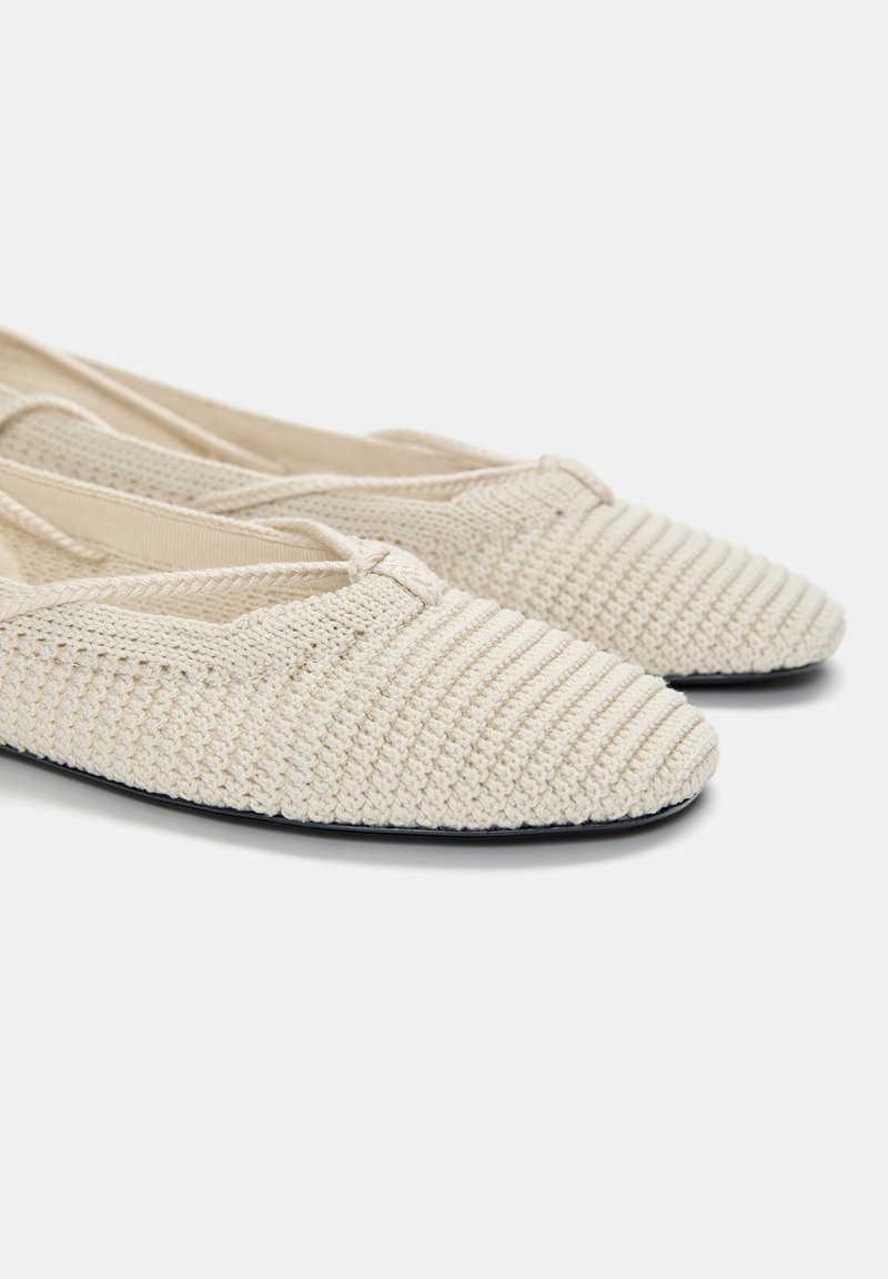 Ballerines en tricot beiges avec un motif texturé et rayé et un léger bout arrondi. Matériau doux et design flexible, semelle plate.