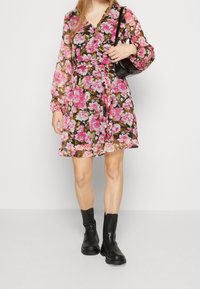 Blommig klänning med svart bakgrund och rosa samt vita blommor, långa ärmar, v-ringning och ett åtsittande midja. Matchad med svarta stövlar.