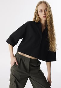 Czarna krótka koszula z wyprofilowanym kołnierzem, z guzikami i krótkim rękawem, zestawiona z oliwkowymi spodniami o wysokim stanie z kieszeniami.