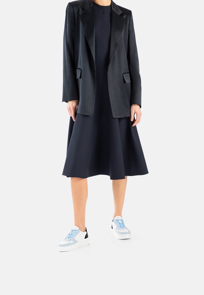 Blazer en satin noir sur une robe swing bleu marine ; associé à des baskets bleu clair et blanches avec des accents noirs.