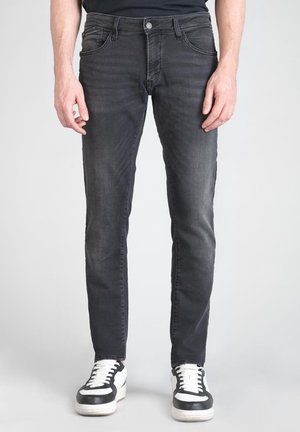 Black denim jeans with a slim fit, featuring front pockets, a zip fly, and slight fading. Paired with black and white sneakers.