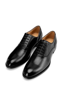Zwarte leren dresschoenen met een gladde afwerking, voorzien van een spitse neus en zes paar veteroogjes voor een verstelbare sluiting.
